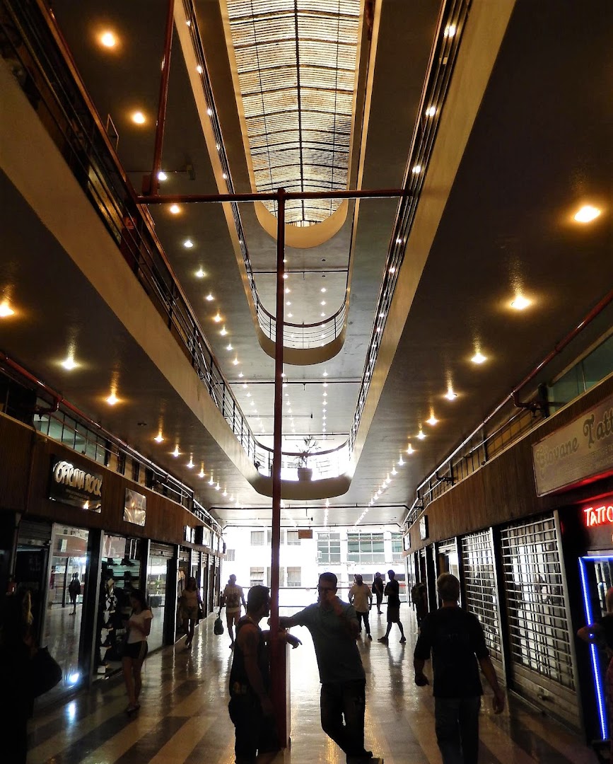 People walking through a brightly lit indoor shopping arcade with multiple levels and shops.