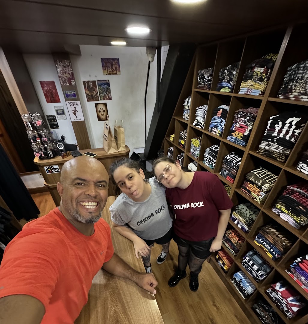 Three people smiling and posing for a selfie inside a store filled with band t-shirts.