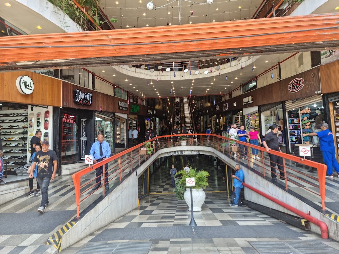 A bustling indoor shopping arcade with various shops and escalators, featuring a unique architectural design.