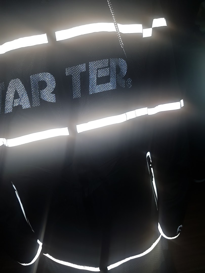 Close-up of a black garment with reflective stripes and the text 'AR TER.'