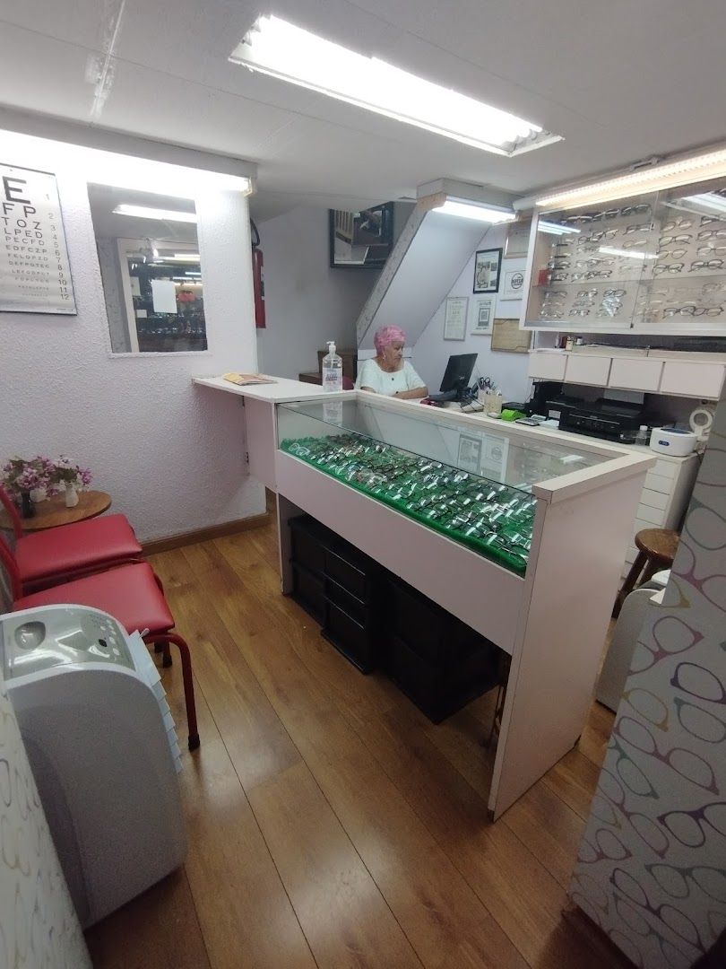 An optician's shop interior with a display of eyeglasses and a staff member at the counter.