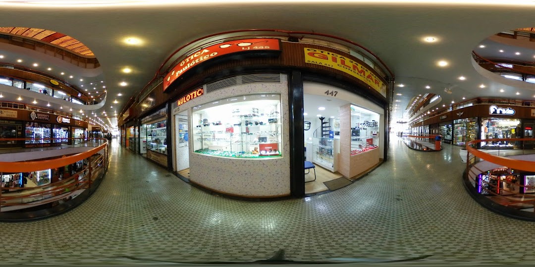 A panoramic view of a shopping mall interior with multiple shops, including an optician.