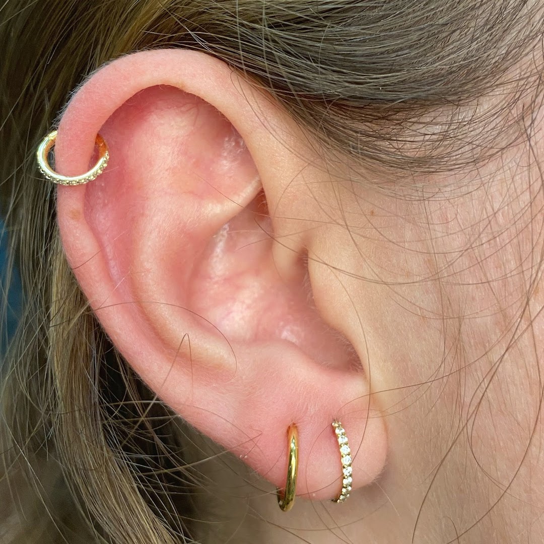 Close-up of a person's ear adorned with multiple gold hoop earrings and studs.