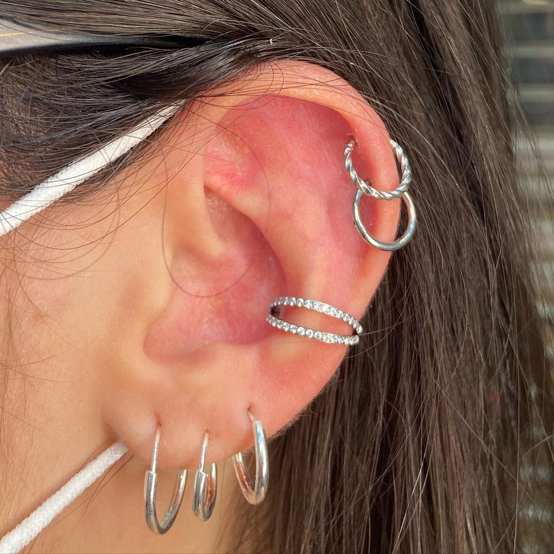 A close-up of a person's ear adorned with multiple silver piercings and earrings.