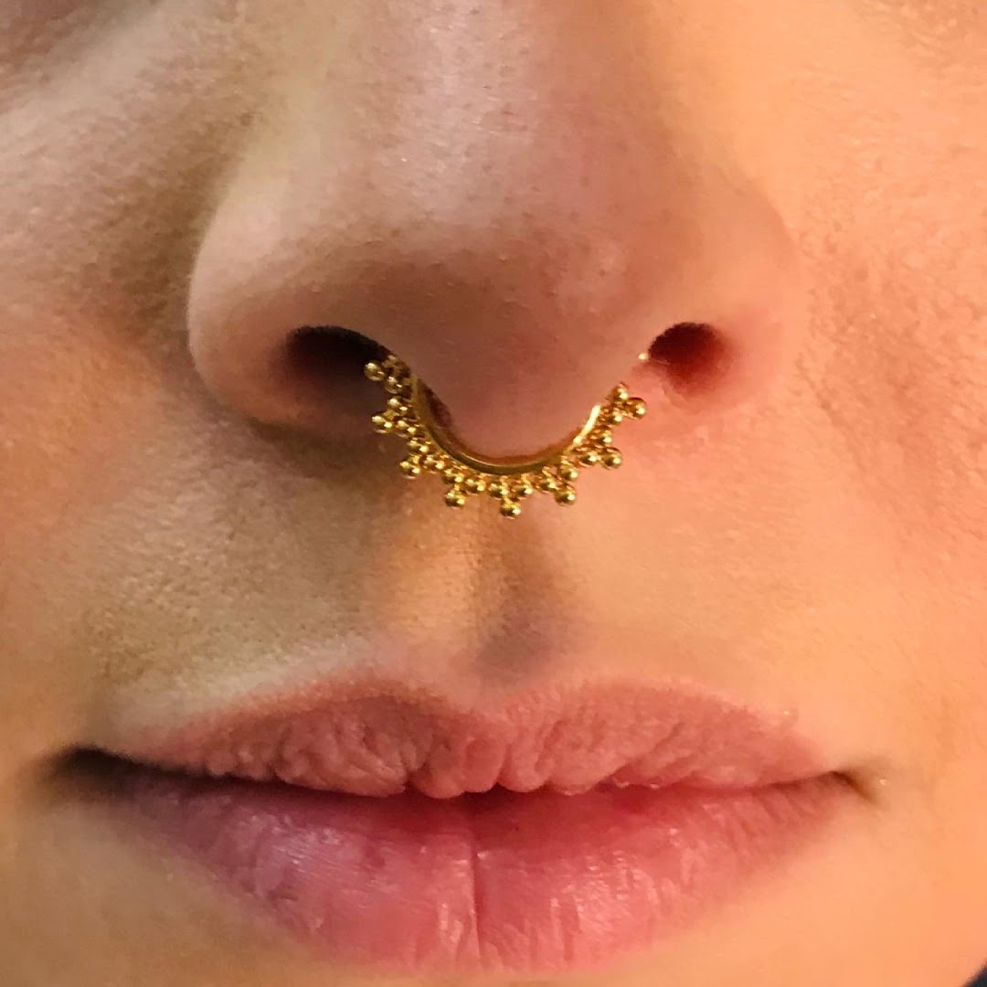 Close-up of a person's nose with a gold septum piercing featuring beaded detailing.