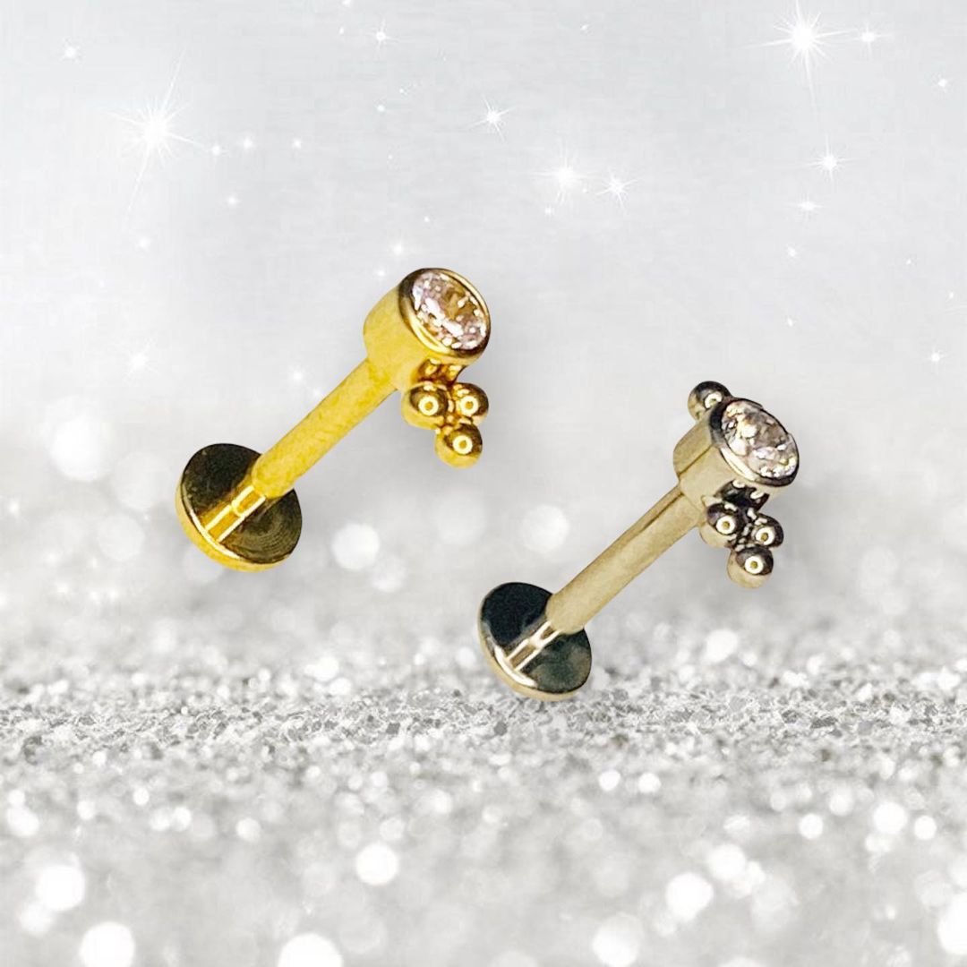 Two sparkling piercings with gemstones and decorative beads on a glittery background.