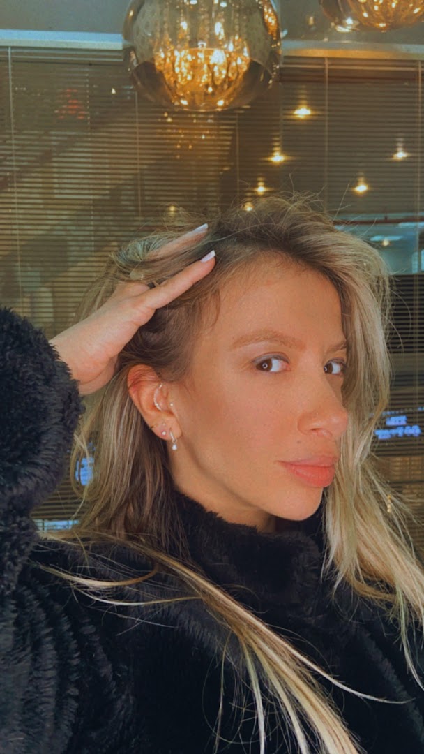 A woman with blonde hair and piercings in her ear, posing for a photo.