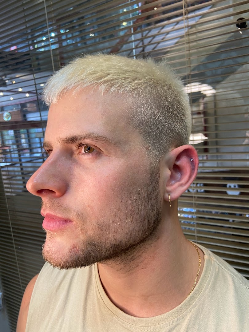 Close-up profile of a man with blonde hair, showing a new ear piercing.