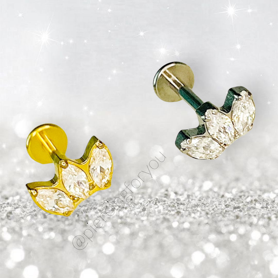 Close-up of two sparkling piercing jewelry pieces with gemstones on a glittery background.