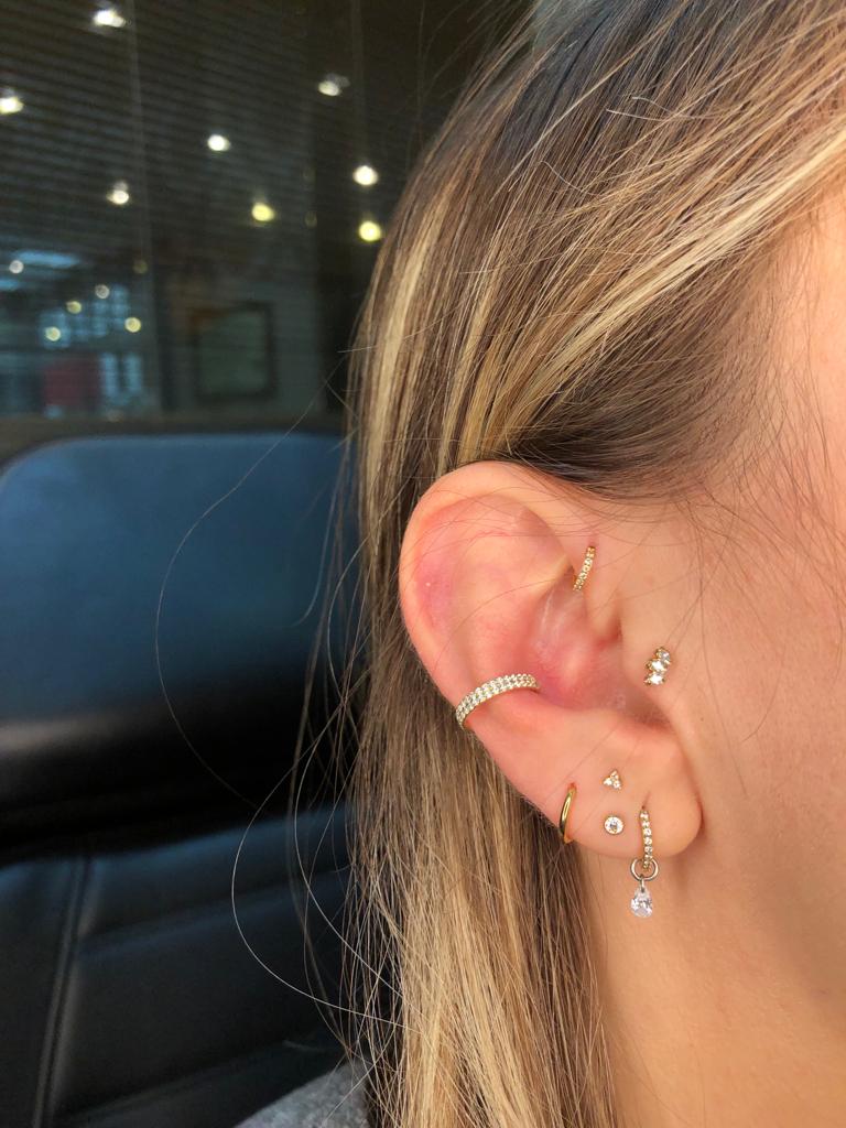 Close-up of a woman's ear adorned with multiple stylish gold and diamond piercings.
