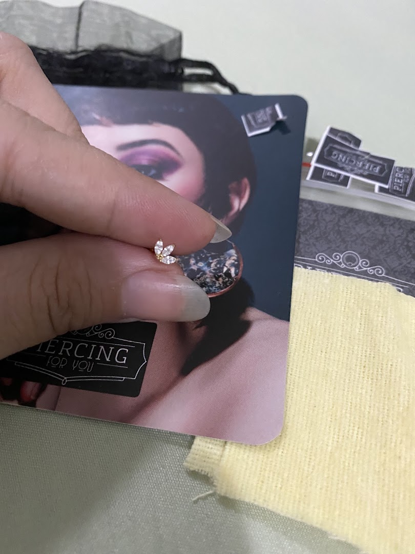 A hand holds a delicate, jeweled piercing stud with a floral design.