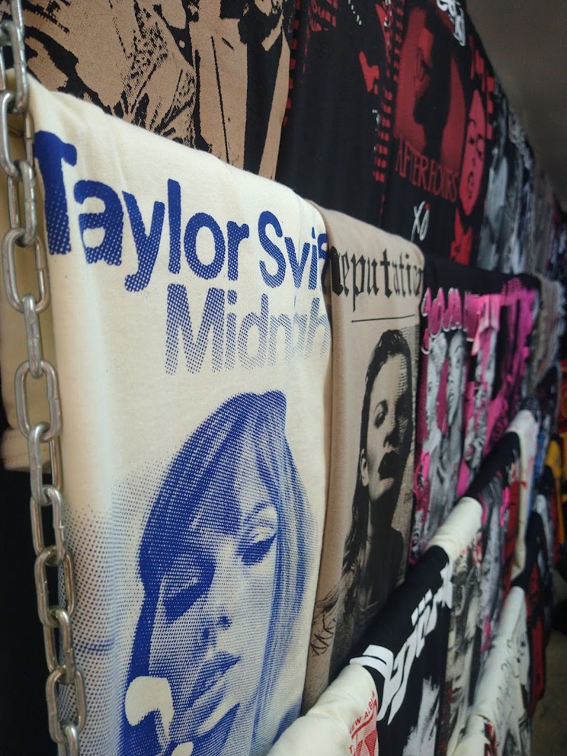 A wall of t-shirts featuring various artists and album art, displayed on chains.