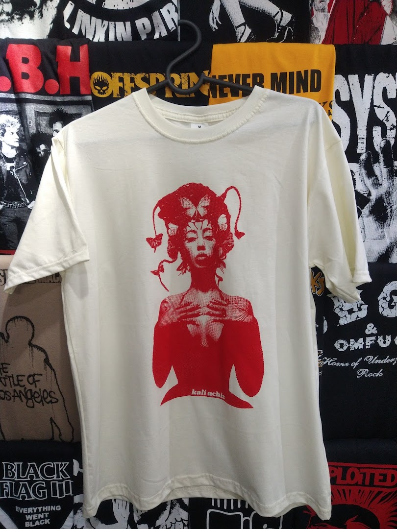 A cream-colored t-shirt with a red graphic of a woman and butterflies, featuring the name 'kali uchis'.