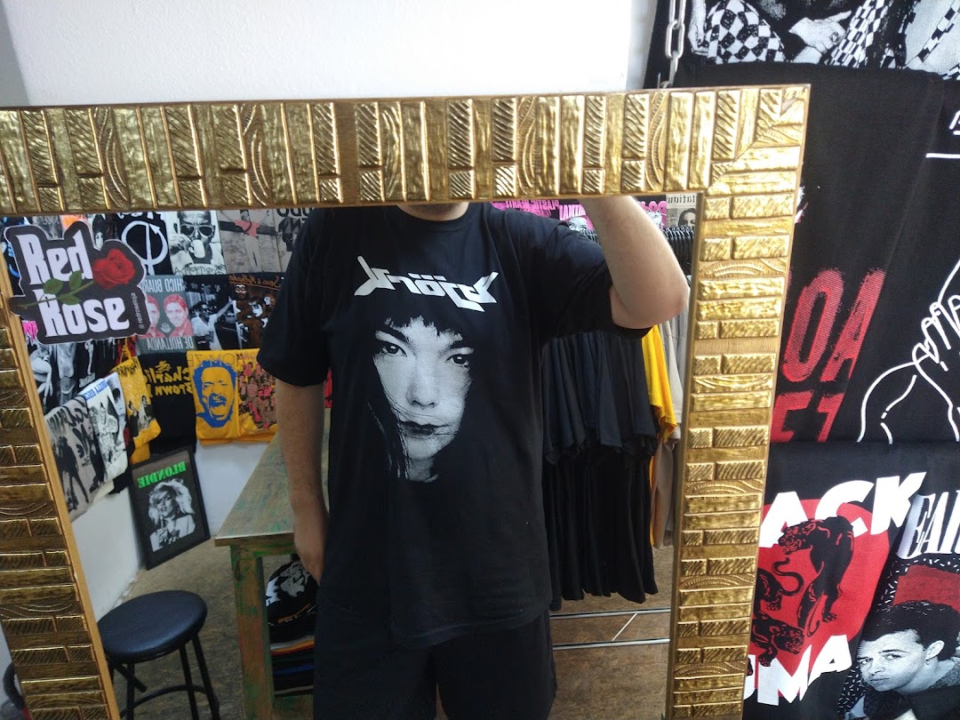 A person wearing a t-shirt with a Bjork portrait is reflected in a gold-framed mirror, surrounded by band t-shirts.