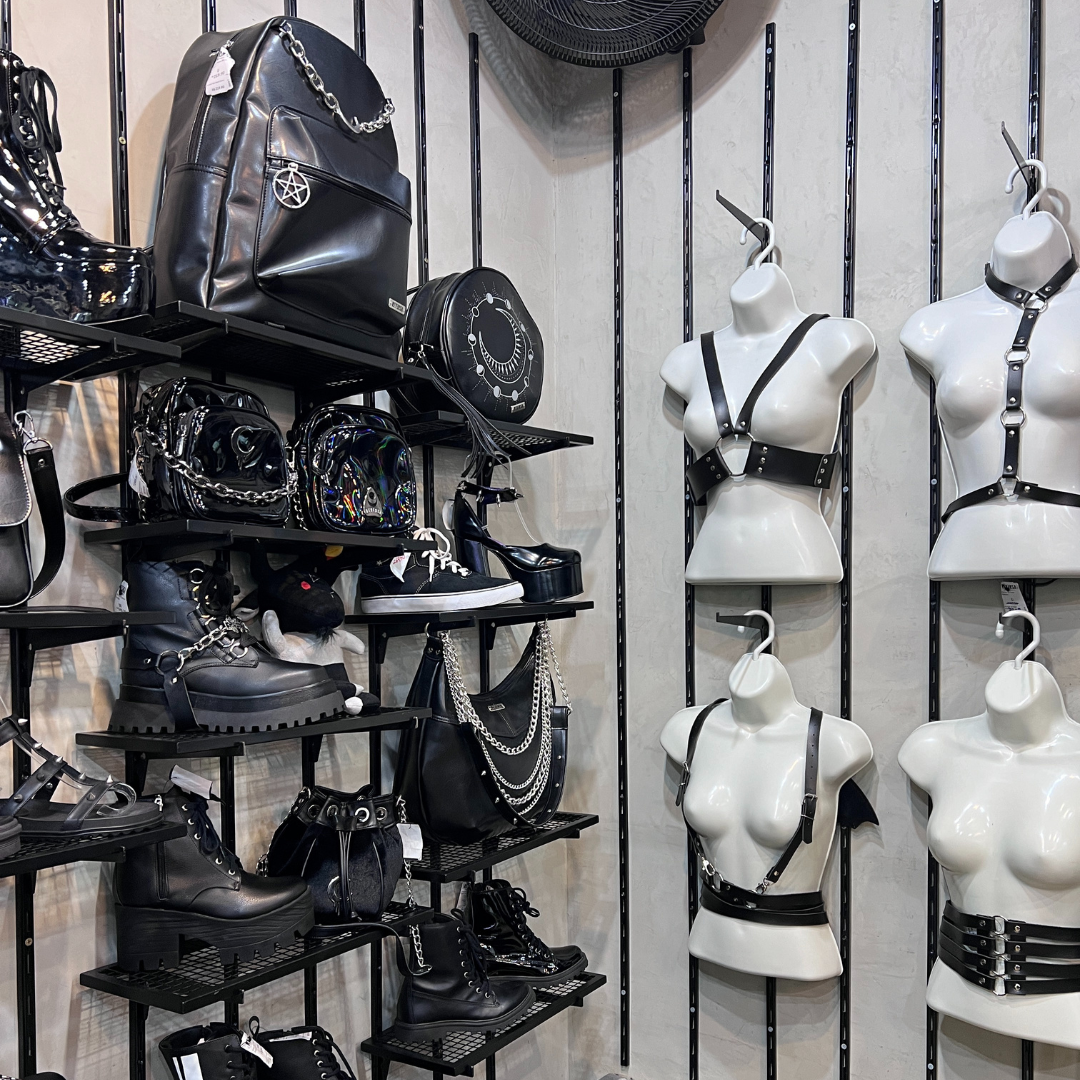 A display of gothic-style fashion accessories including boots, backpacks, and harnesses on shelves.