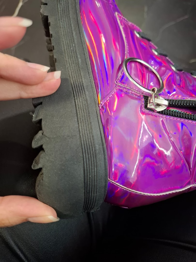 A close-up of a person's hand touching the thick sole of a shiny purple holographic boot.