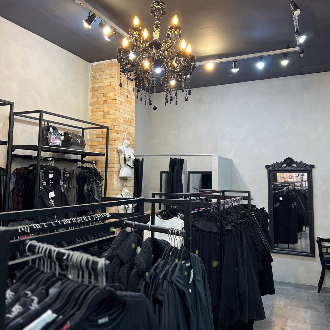 Interior of a clothing store with racks of black apparel and a decorative chandelier.
