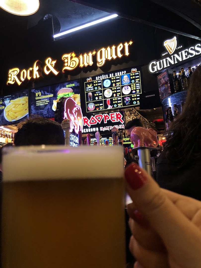 A person holds a beer in the foreground with a bar and menu in the background.