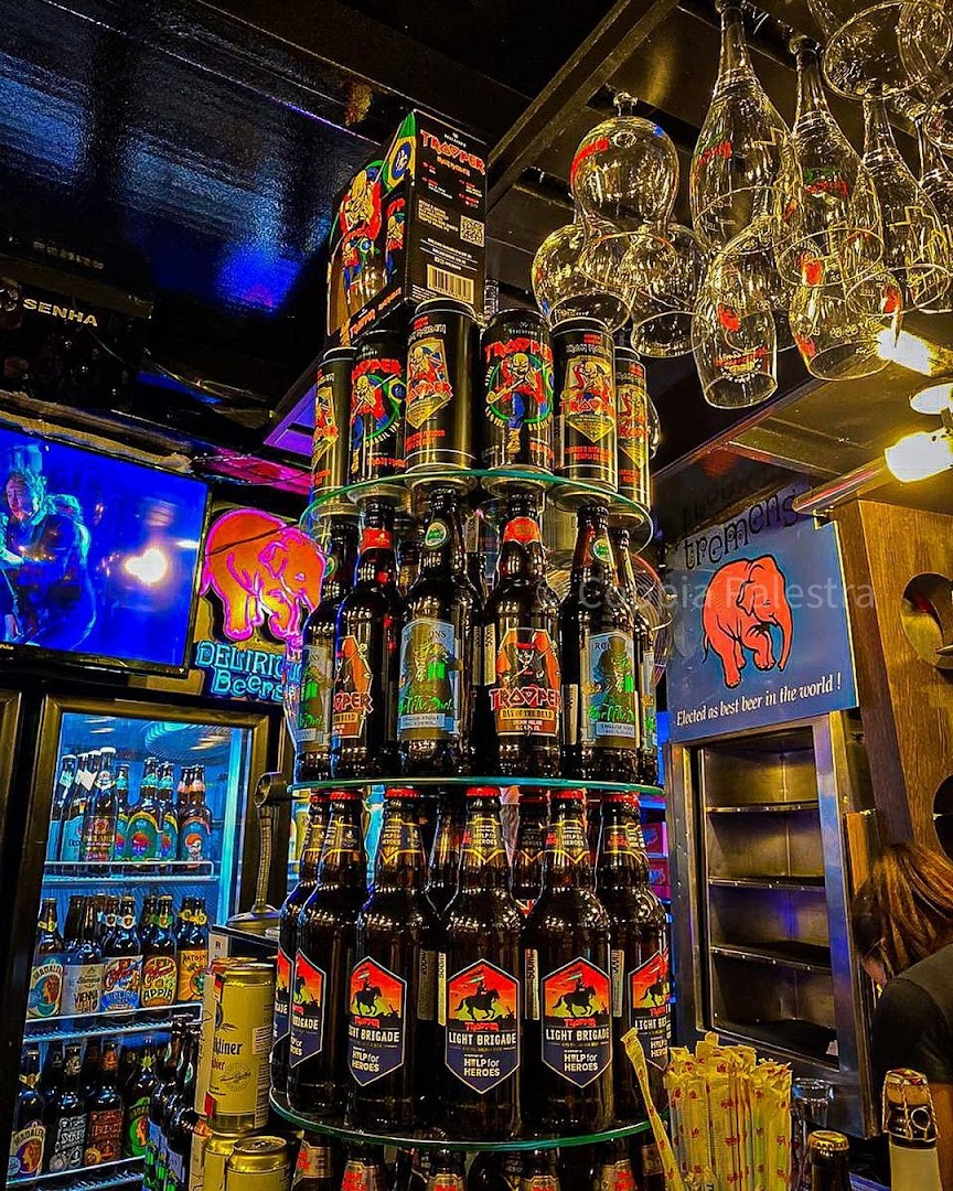 A display of various beers, including bottles and cans, with hanging glasses above.