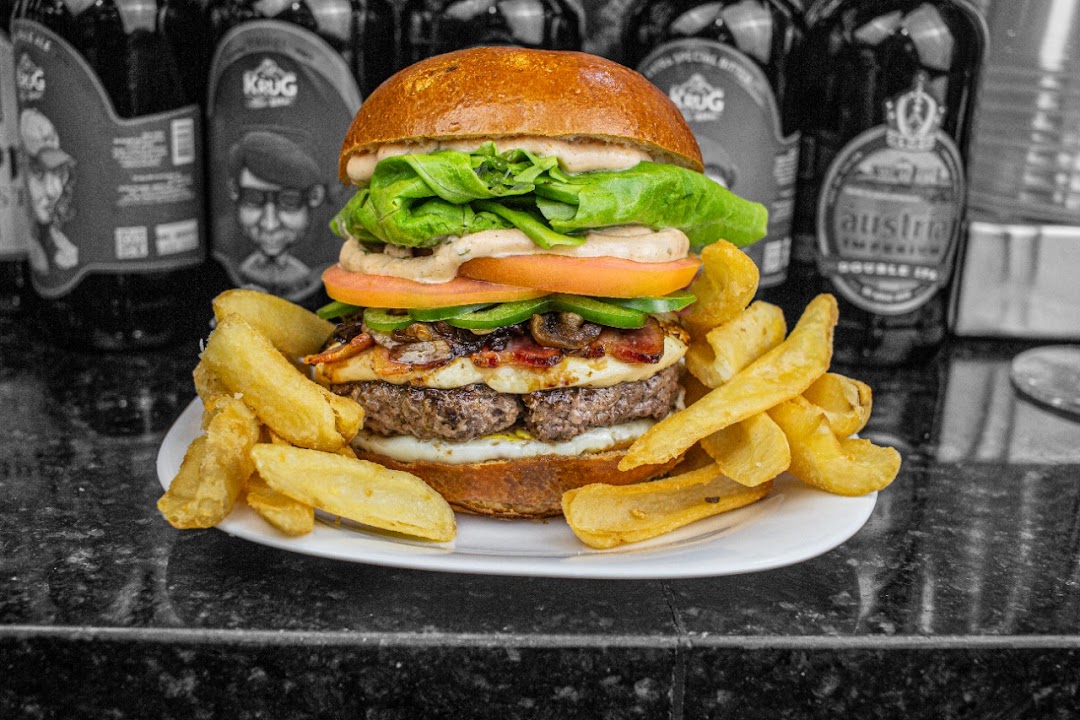 A gourmet burger with fries, presented on a white plate with bottles in the background.