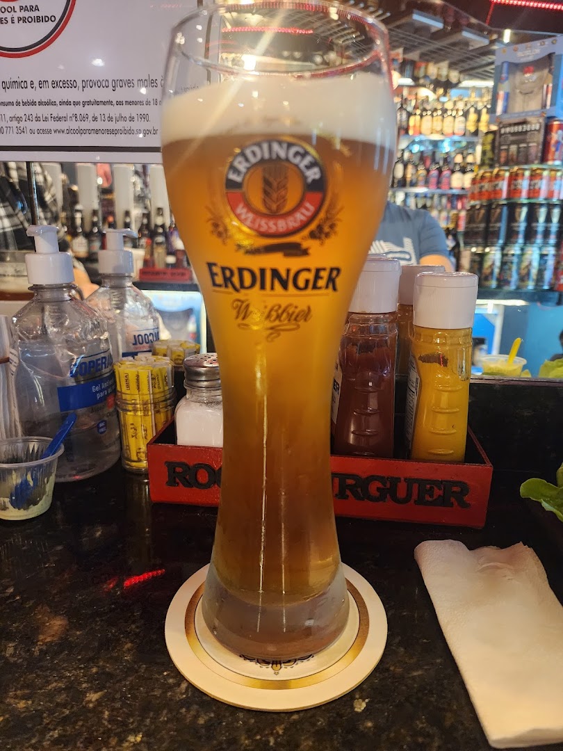 A tall glass of Erdinger Weissbier beer sits on a coaster in front of a bar.