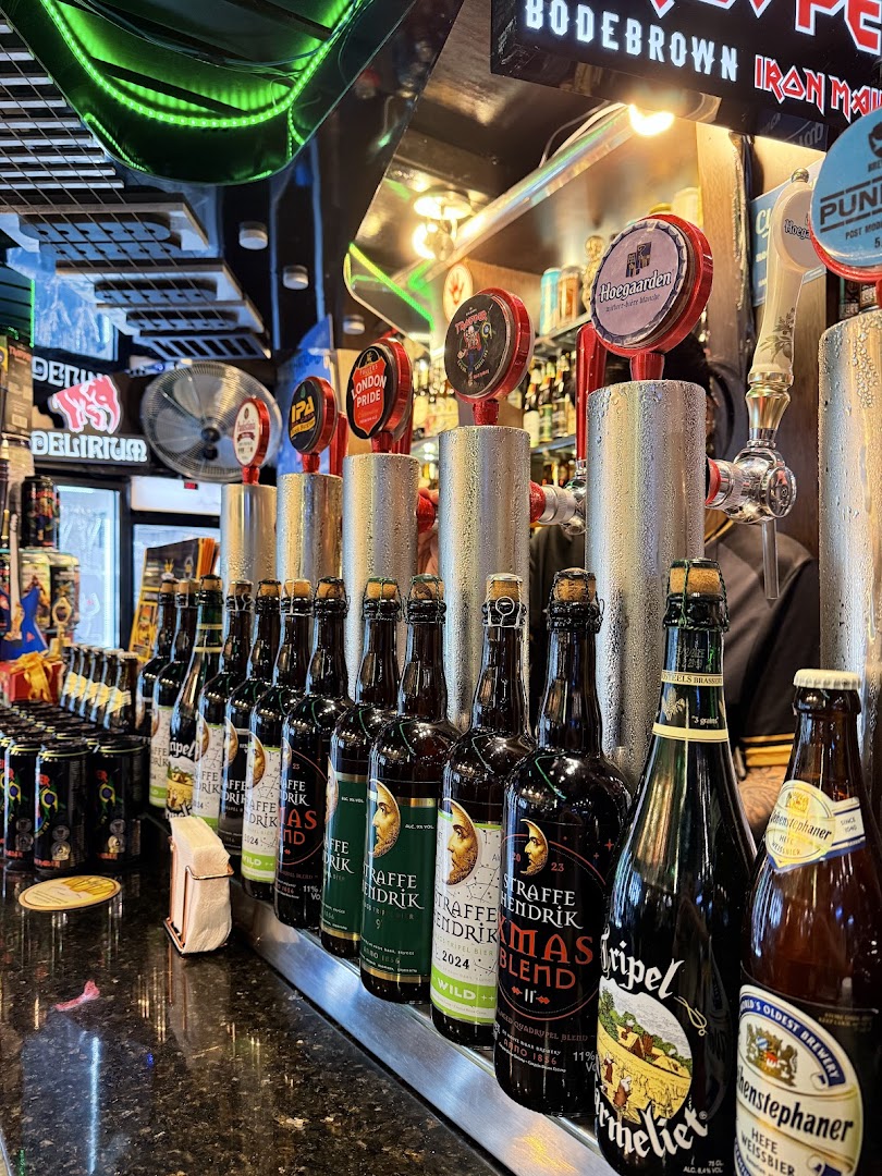 A bar counter displaying a variety of beer taps and bottles, with neon signs in the background.