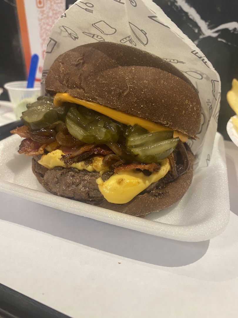 A close-up shot of a gourmet burger with pickles, bacon, and melted cheese.