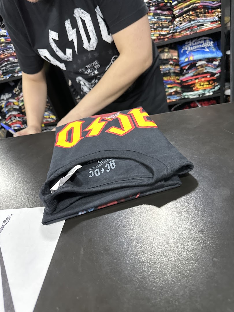 A person wearing an AC/DC t-shirt folds another AC/DC t-shirt on a counter.