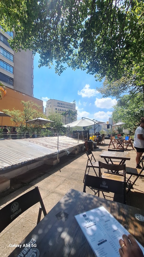 Rooftop dining area with tables, chairs, umbrellas, and city buildings in the background.
