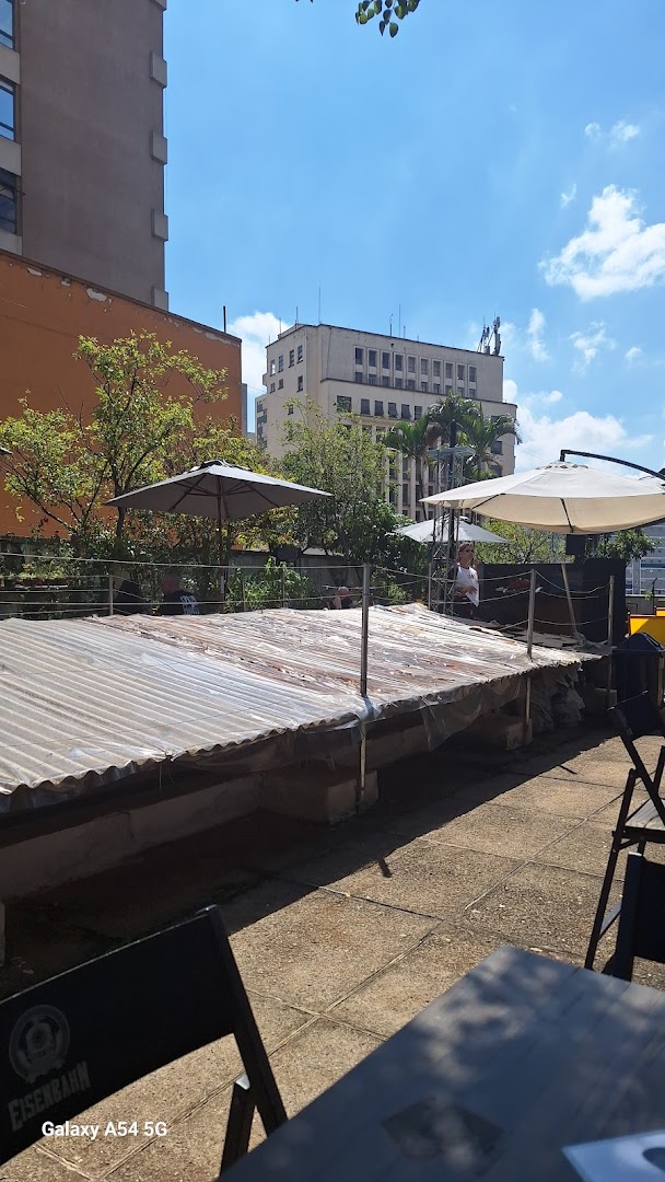 Outdoor seating area with corrugated roof, umbrellas, and city buildings in the background.