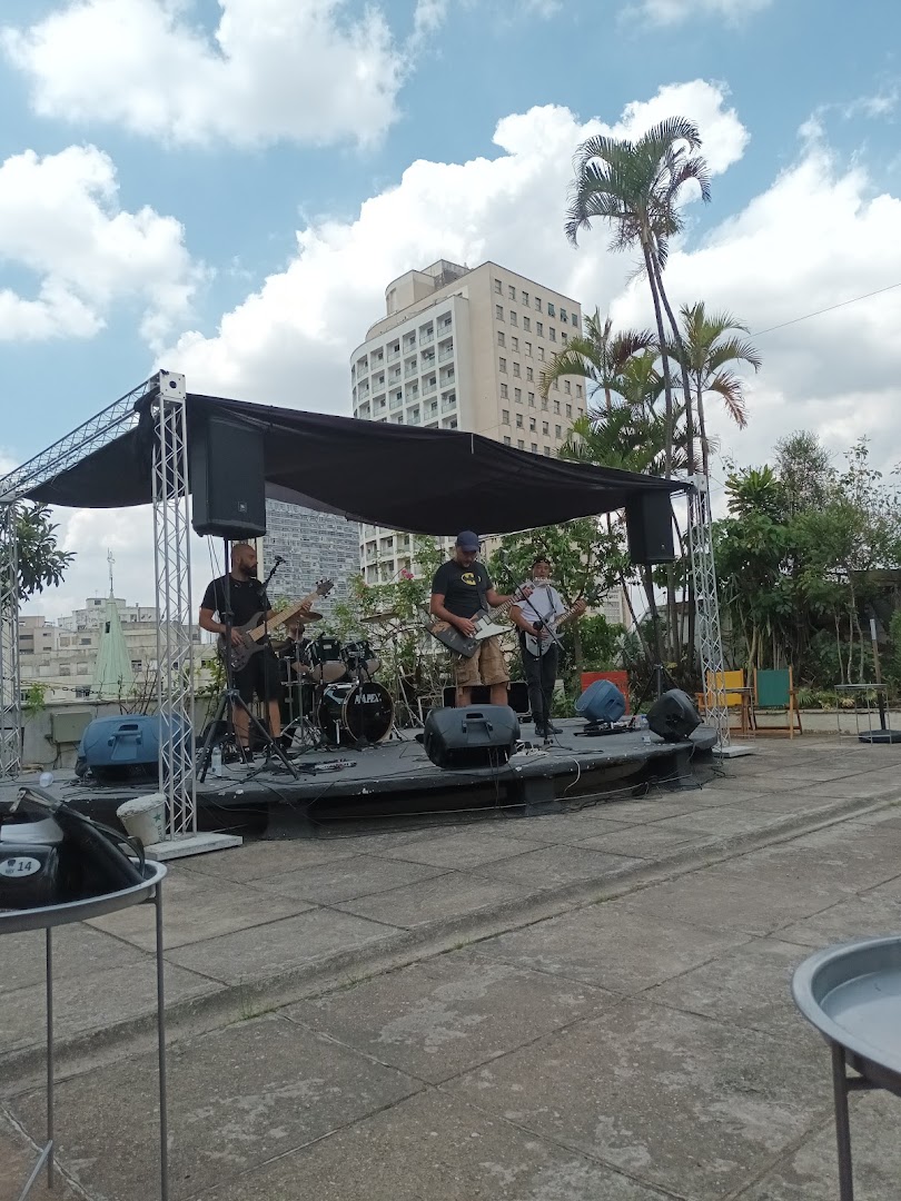 A band performs live music on an outdoor stage with buildings and palm trees in the background.