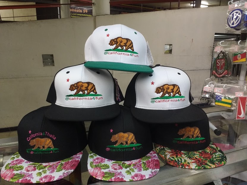 A display of California-themed baseball caps with bear logos and various brim designs.