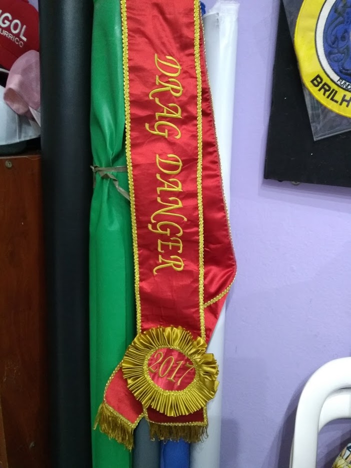 A red sash with gold trim and embroidery that reads 'DRAG DANGER' and '2017'.