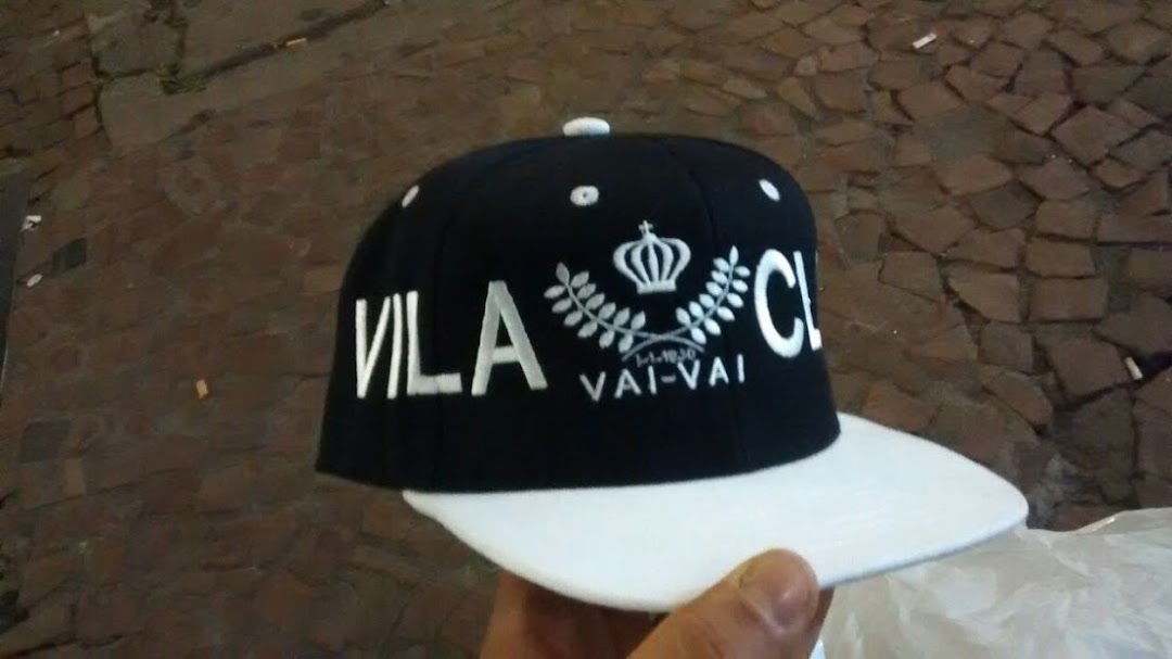 A black and white baseball cap with 'VILA' and 'VAI-VAI' text and a crown emblem.