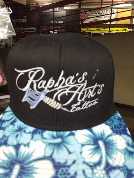 A black baseball cap with 'Rapha's Art's Tattoo' embroidered in white, featuring a tattoo gun.
