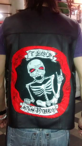 A person wearing a black leather vest with a large embroidered patch of a skeleton.