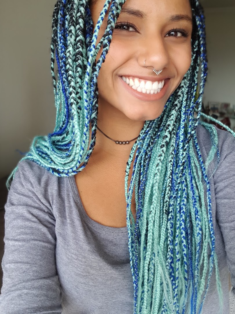 A smiling woman with colorful blue and teal box braids and a septum piercing.