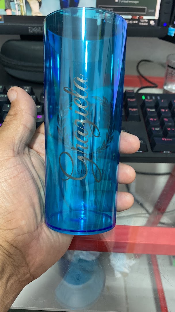 A hand holds a personalized blue glass with elegant script lettering and floral accents.