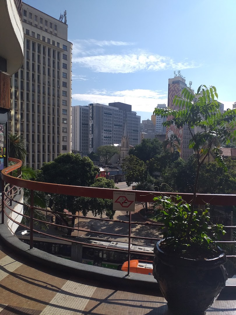 View from a balcony overlooking a city street with buildings, trees, and a bus.