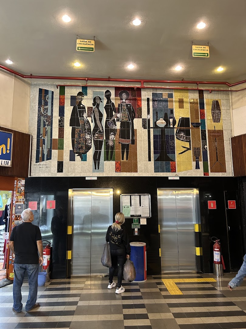 People stand near elevators in a building with a colorful tiled mural.