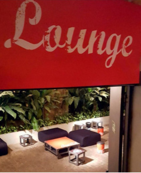 A lounge area with comfortable seating, tables, and lush greenery.