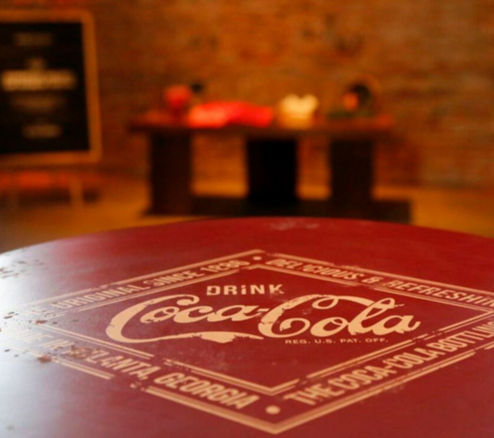 A close-up of a red table with a vintage Coca-Cola logo, with a blurred background of a shop interior.