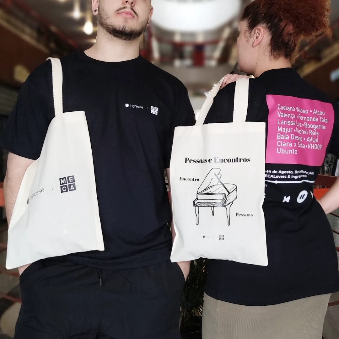 Two people wearing branded t-shirts and holding tote bags with event details.