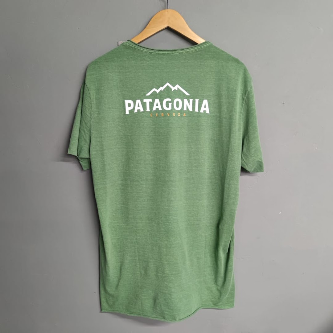 A green t-shirt with the Patagonia Cerveza logo hanging on a wooden hanger.