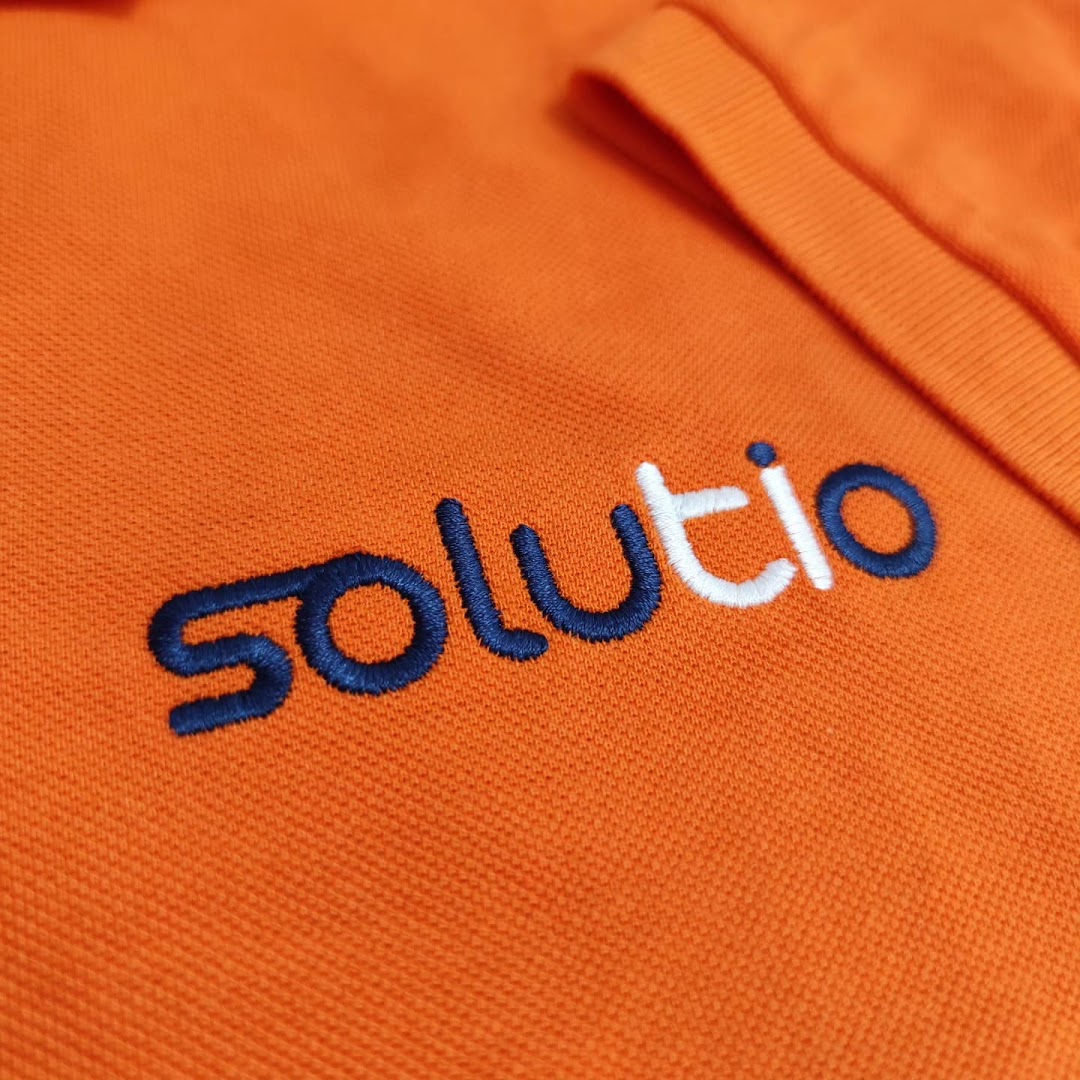 Close-up of an orange polo shirt with embroidered 'solutio' logo in navy and white.