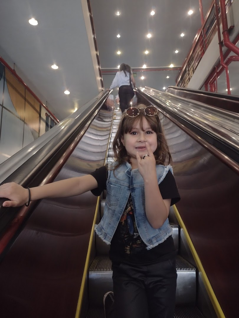 A young girl with sunglasses on her head rides an escalator, looking at the camera.