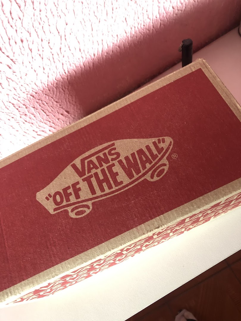 A close-up of a red Vans shoe box with the iconic 'Off The Wall' logo.
