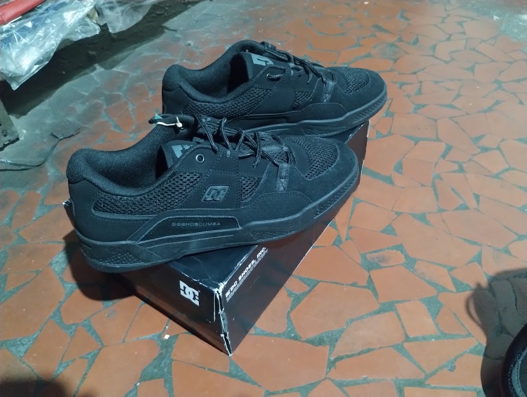 A pair of black DC Shoes sneakers are displayed on top of their branded box.