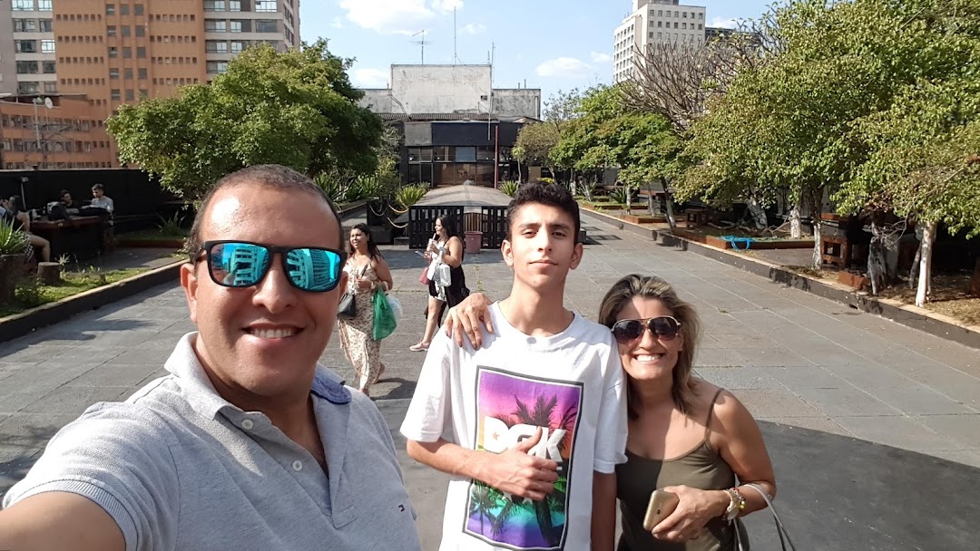 A family smiles for a selfie in an outdoor plaza with trees and buildings in the background.