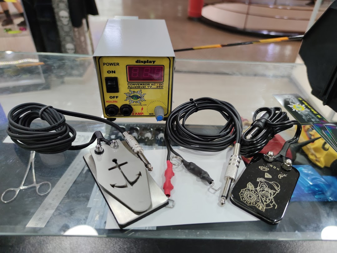 Tattoo machine power supply, foot pedals, and cables displayed on a glass surface.